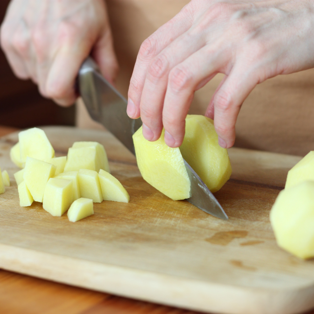 raw potatoes being cut with knife on wooden chopping board